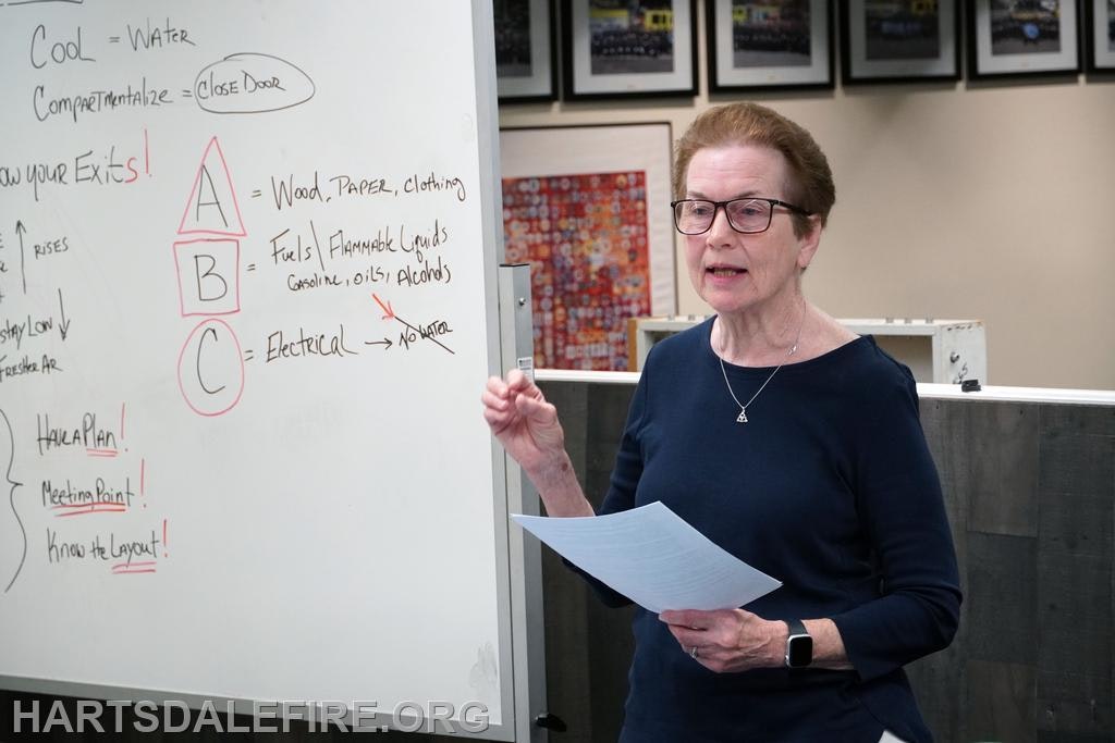 A person giving a presentation. Whiteboard with fire safety tips like "cool," "compartmentalize," and types of fires (A, B, C).