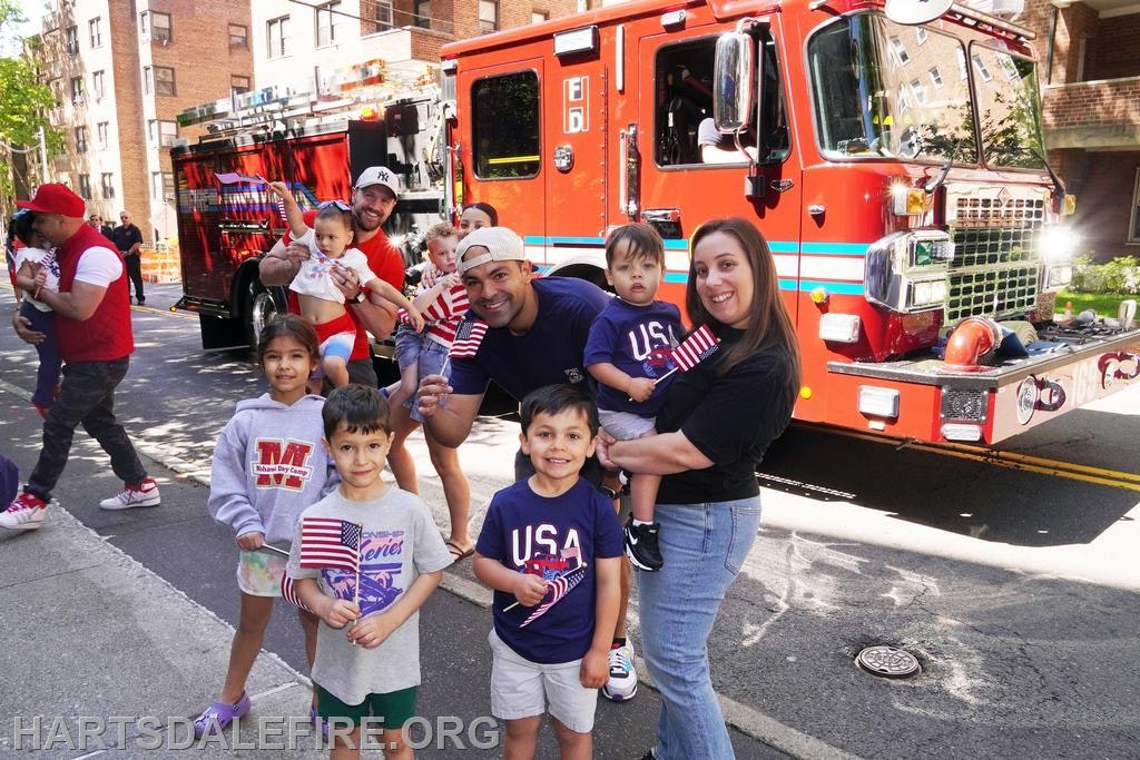 A group of adults and children posing in front of a colorful fire truck, celebrating with American flags.