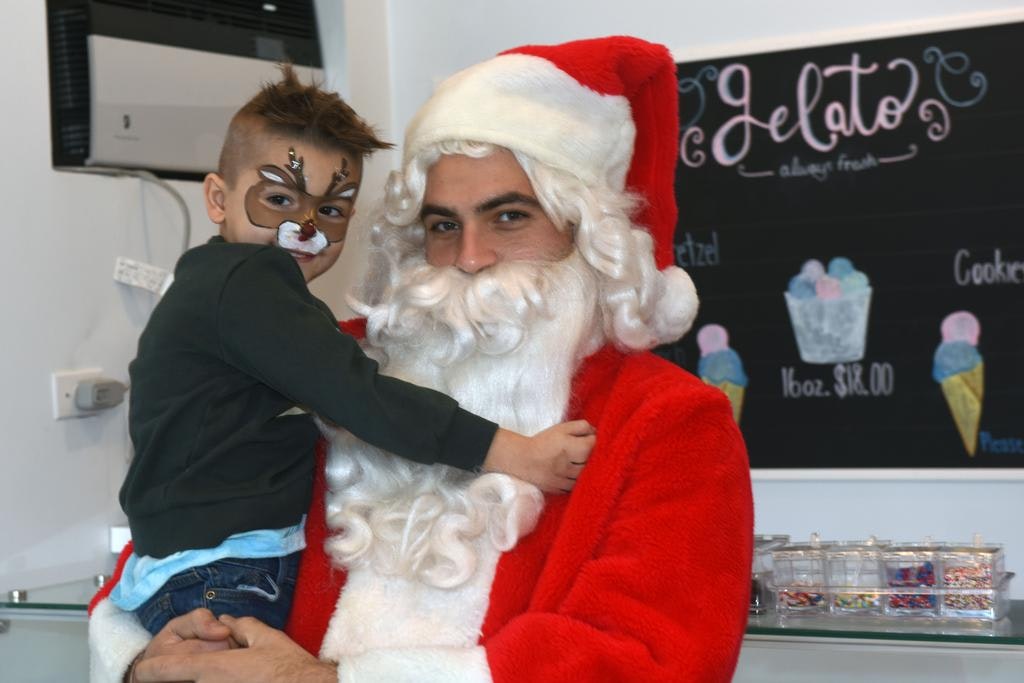 A child with face paint hugs a man dressed as Santa Claus in an ice cream shop.