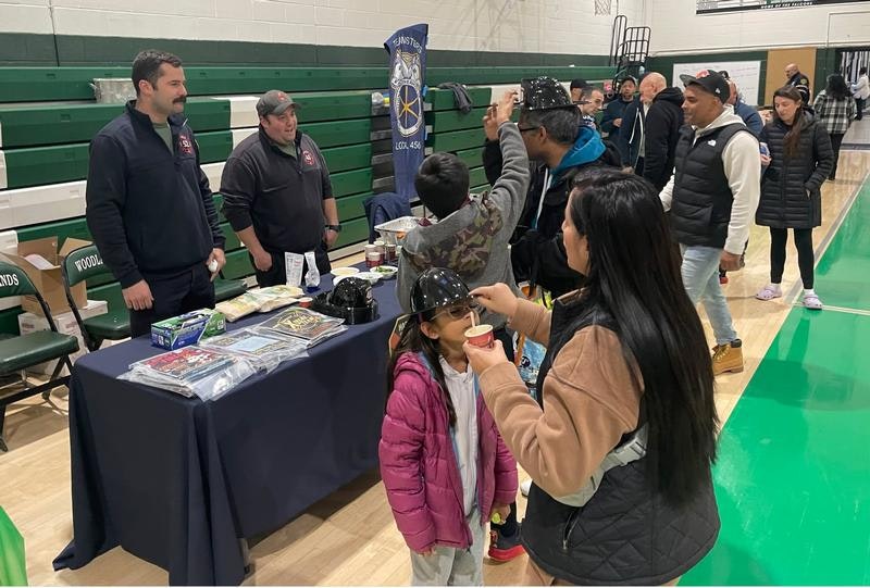 A community event with kids and adults interacting at a table, possibly for safety or education, with informational materials displayed.