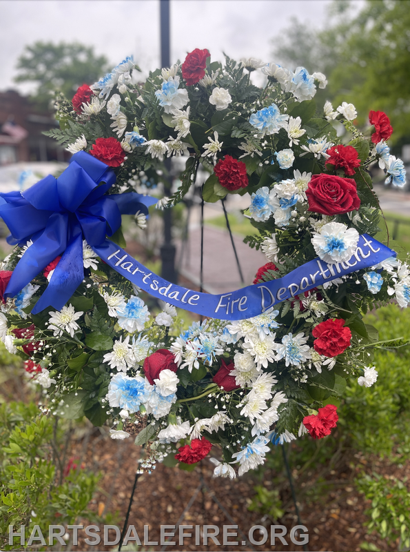 A floral wreath featuring red and blue flowers, with a blue ribbon that reads "Hartsdale Fire Department."