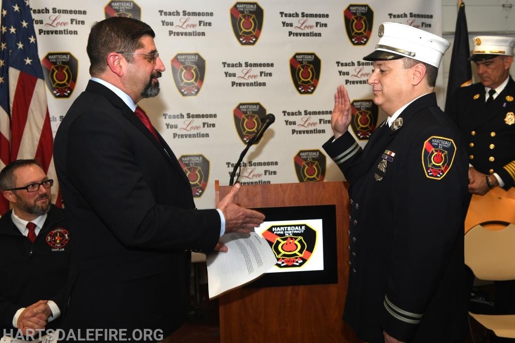 A firefighter takes an oath at a ceremony with "Teach Someone You Love Fire Prevention" backdrop.