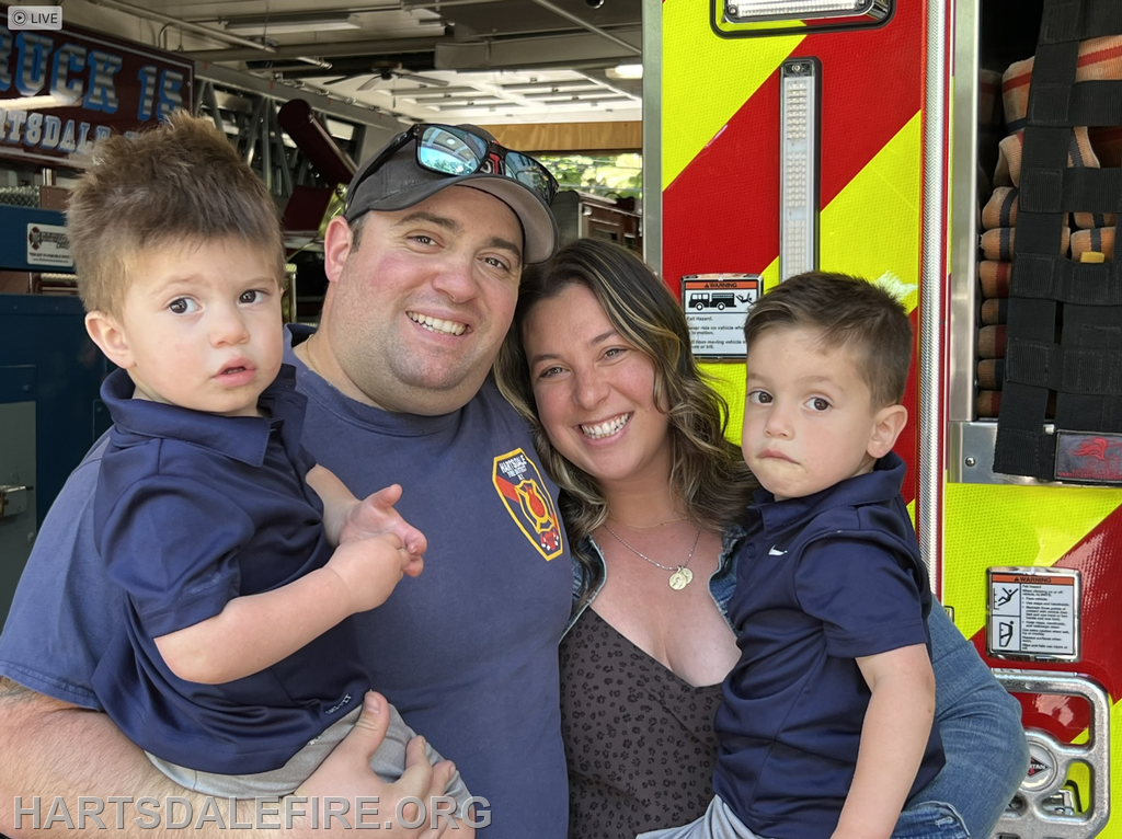 A smiling family portrait with two young boys, a woman, and a man in front of a fire truck.