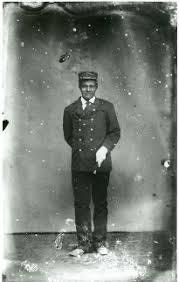 A person in a uniform and cap stands against a plain backdrop.