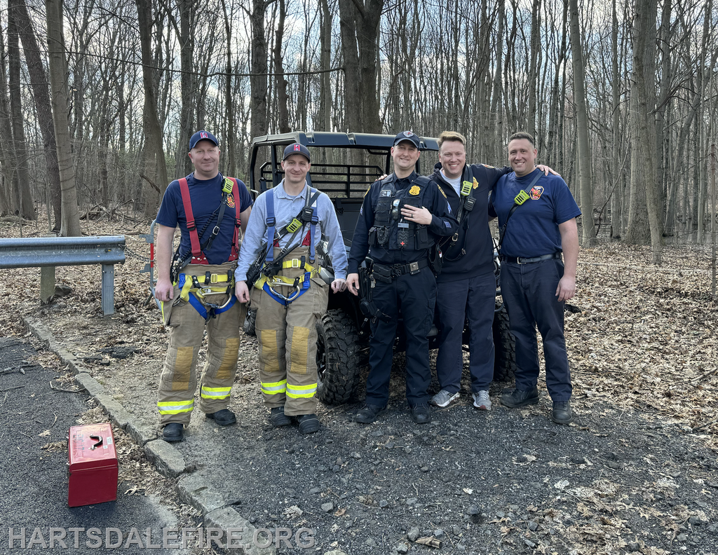 A group of emergency responders poses together in a wooded area next to an all-terrain vehicle, showcasing teamwork and readiness.