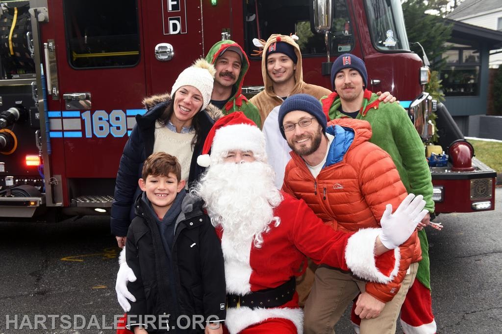 A festive group poses with Santa in front of a fire truck, celebrating the holiday spirit.