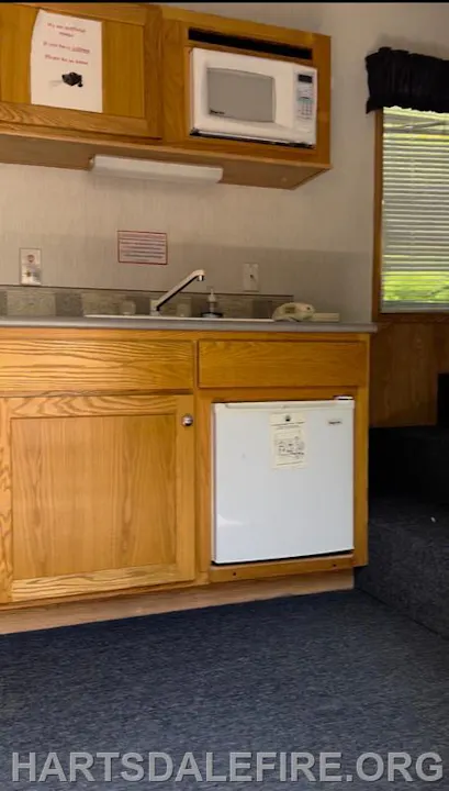 A small kitchen area with a microwave, sink, countertop, and mini-fridge.