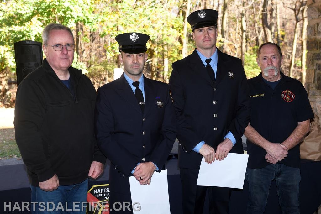 The image shows four men: two in fire uniforms, one in casual wear, and one in a commissioner shirt, likely at an event.