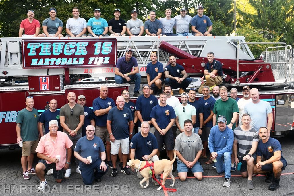 A group photo of firefighters from Hartsdale Fire Department, posing with their fire truck and a dog.