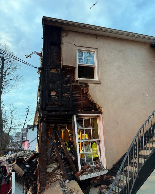 The image shows a building with significant fire damage on one side, revealing exposed wood and debris near the foundation.