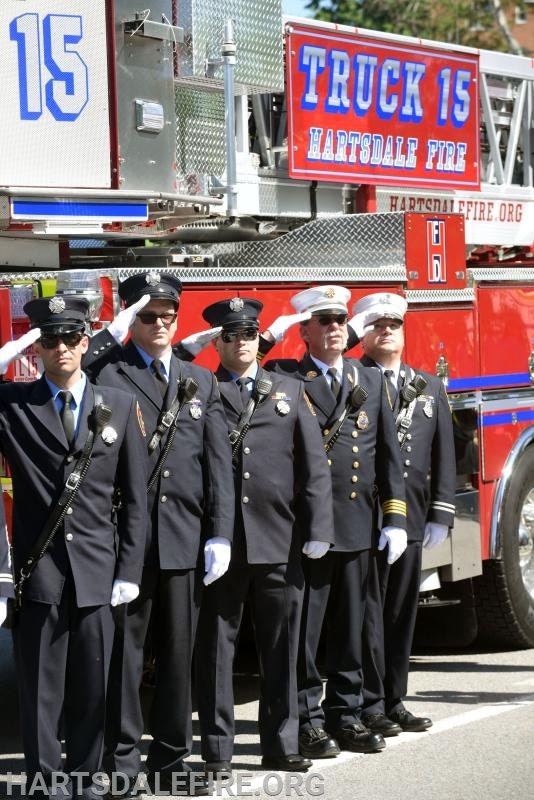 Firefighters in uniform saluting in front of Hartsdale Fire Truck 15.