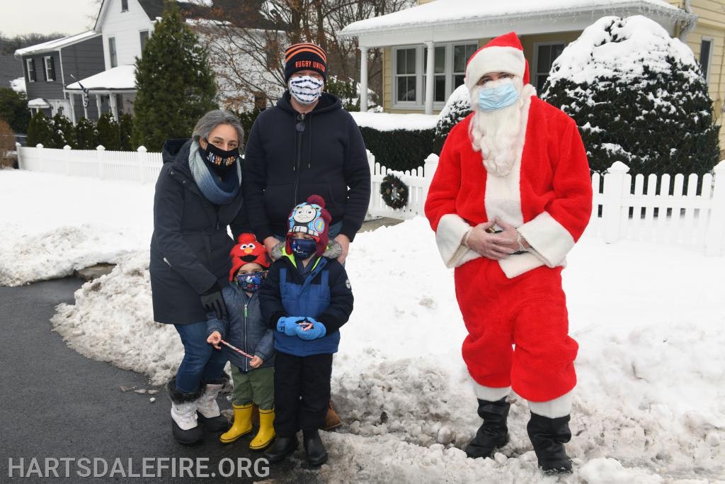 A family with kids in winter clothing and a person dressed as Santa, all wearing masks, standing in the snow.