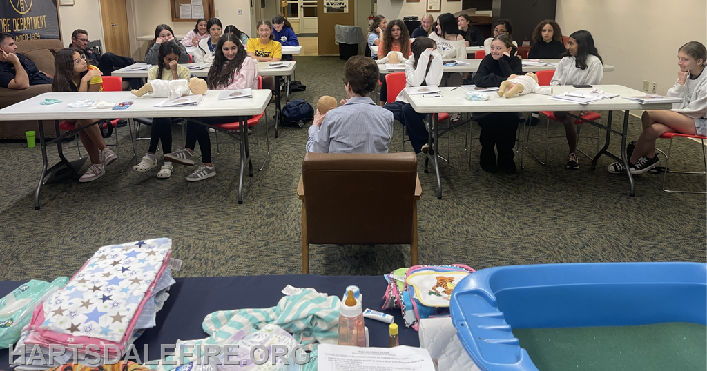 A group of students is attending a class on caregiving, using dolls and teaching materials in a classroom setting.