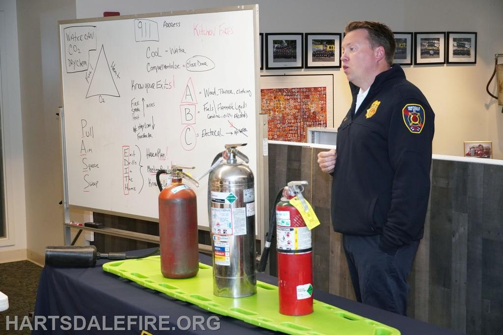 Fire safety demonstration with a firefighter, whiteboard, and fire extinguishers.