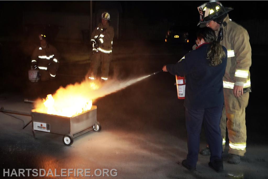 A fire training session in progress, with one person using a fire extinguisher to put out flames while others observe.