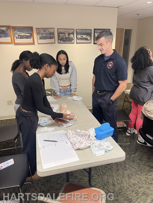 A group is practicing infant care techniques using a mannequin, guided by an instructor.