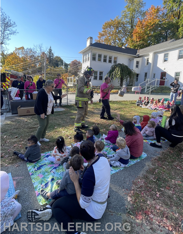 A firefighter interacts with children and adults at an outdoor event, promoting safety and community engagement.