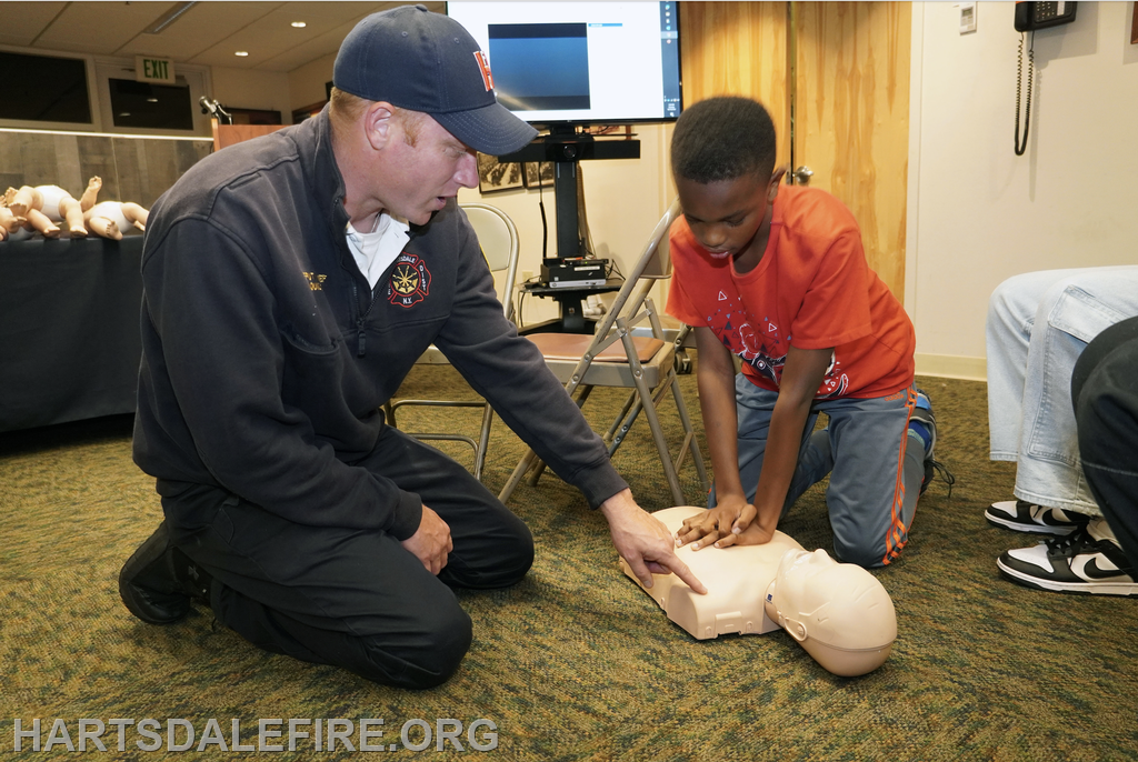 A firefighter teaches a child CPR on a practice dummy during a training session.