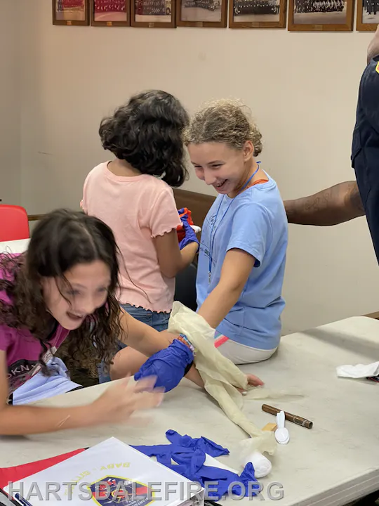 Children laughing and playing with gloves at a table in a classroom setting.