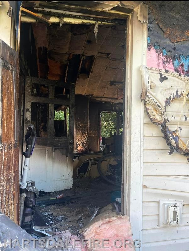 A fire-damaged room with charred walls and debris visible through an open door.