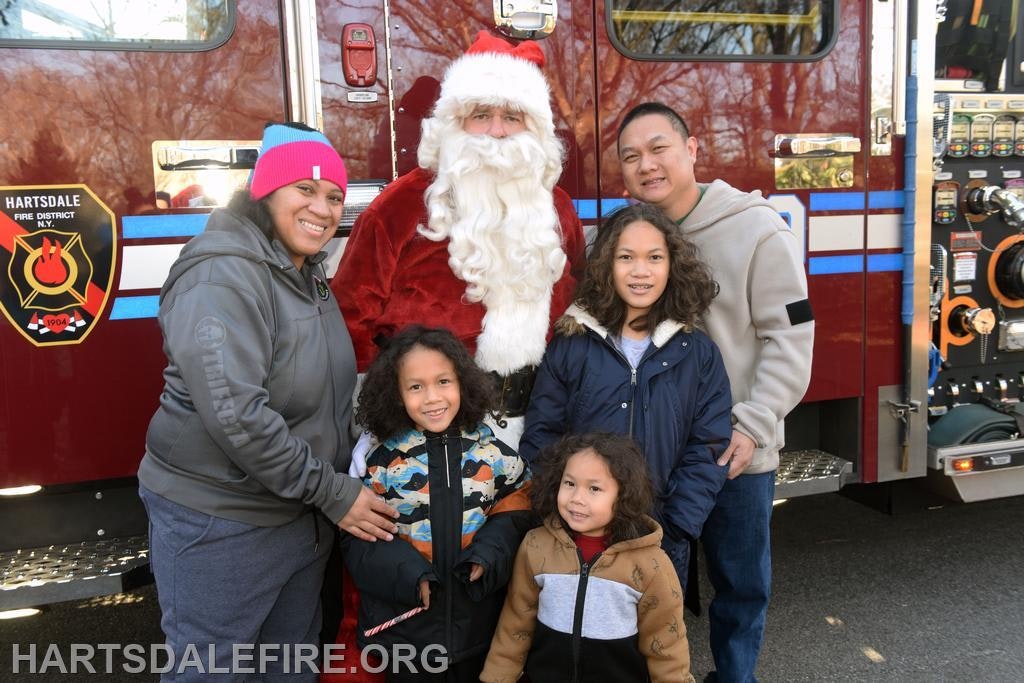 A family poses with Santa Claus in front of a fire truck during a festive event.
