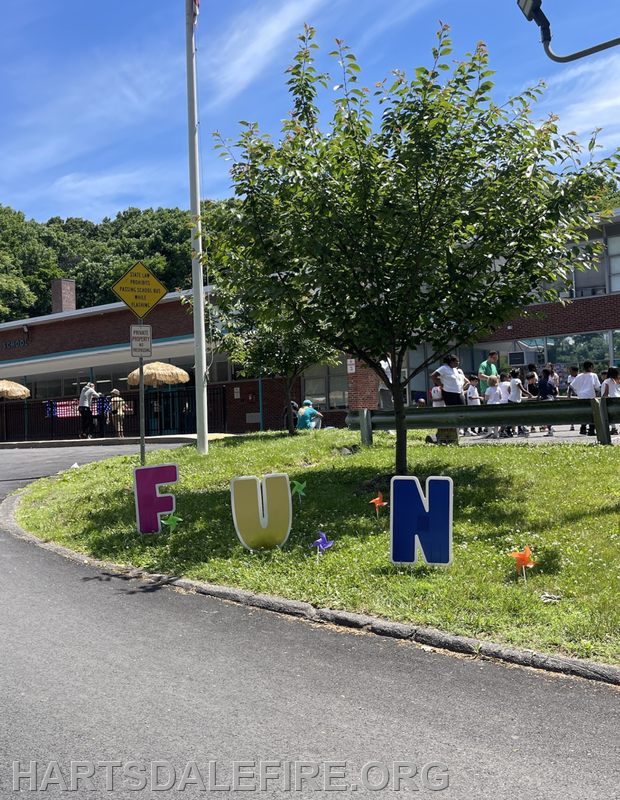 A vibrant school scene featuring colorful letters spelling "FUN," with students outside and a tree nearby.