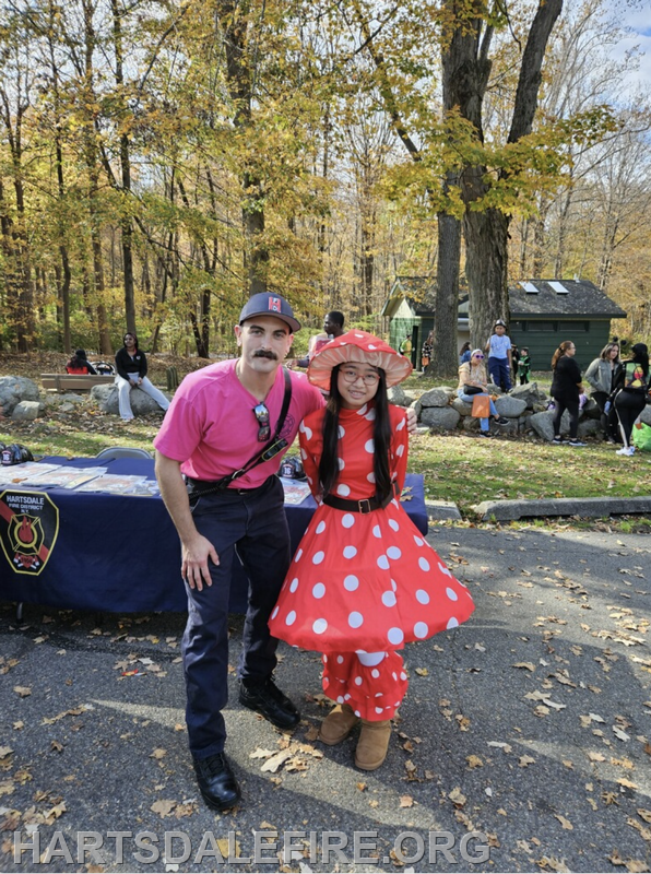 A man in a pink shirt and a girl in a polka-dot dress pose together in a colorful autumn park setting.