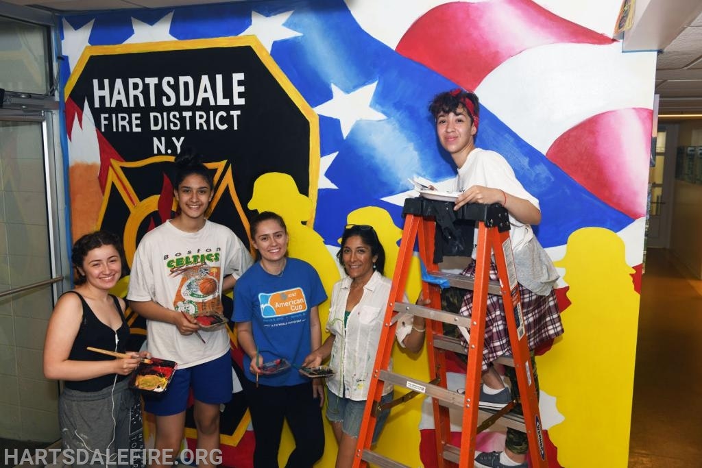 A group of people painting a mural with the Hartsdale Fire District logo and a flag motif in the background.
