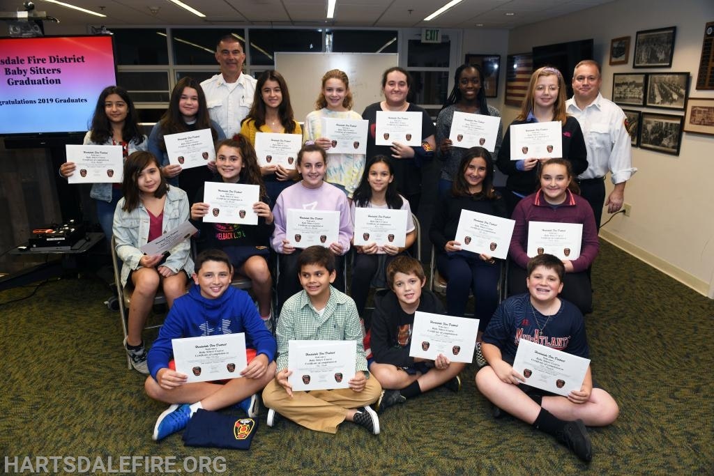 A group of kids holding certificates at a babysitter graduation with two adults.