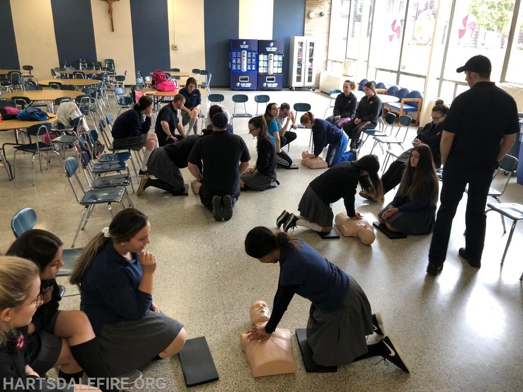 A group of people in a room practicing CPR on mannequins, supervised by instructors.