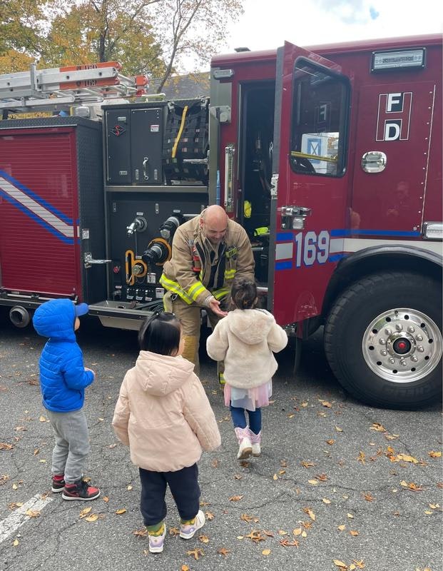 A firefighter interacts with young children near a fire truck, creating an engaging learning experience.
