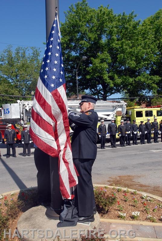 A firefighter is raising the American flag while fellow firefighters stand in formation, honoring the occasion.