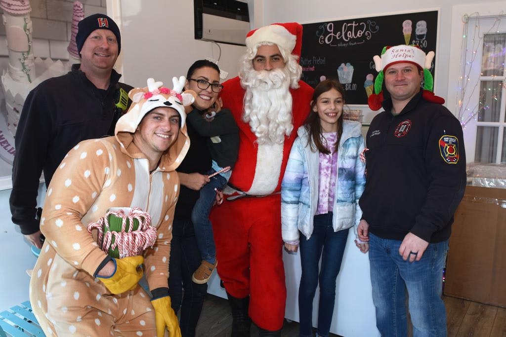 A group of people posing with someone dressed as Santa Claus and another in a reindeer onesie holding candy canes, in a festive setting.