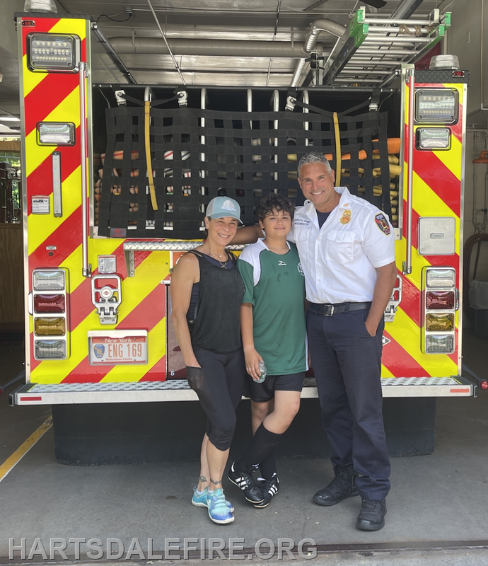A woman, a boy, and a firefighter pose together in front of a fire truck, showing community engagement and support.
