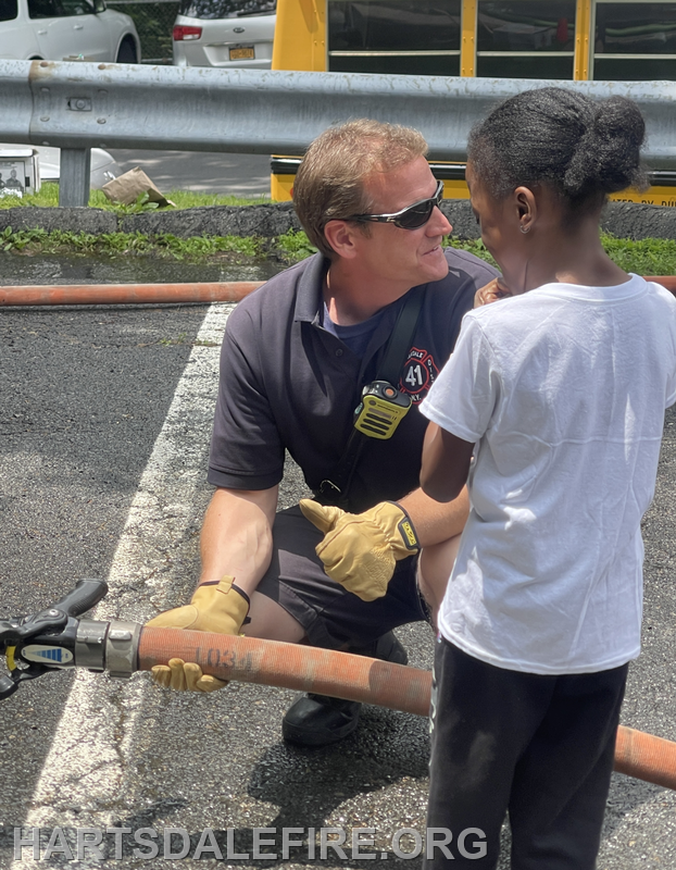 A firefighter interacts with a child, holding a fire hose, in a friendly and engaging manner.