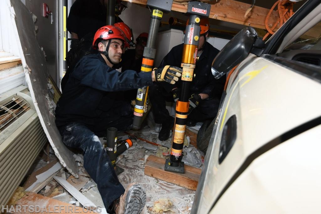 Rescuers in helmets stabilize a structure using poles after a vehicle crash into a building.