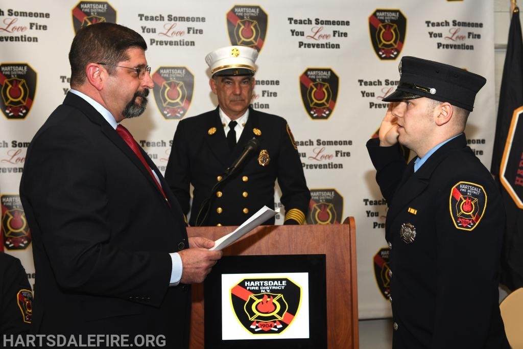 A firefighter taking an oath, with officials present, in front of a Hartsdale Fire District banner.
