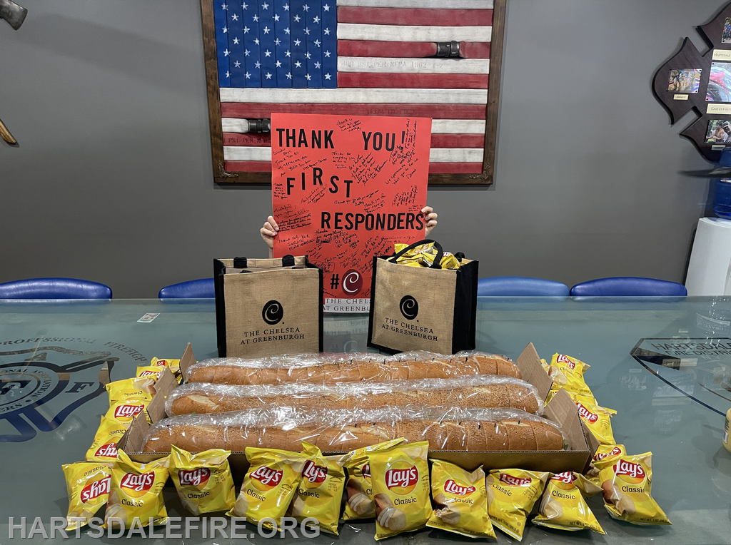 A thank-you sign for first responders, surrounded by bags of chips and sandwiches on a table in a fire station.