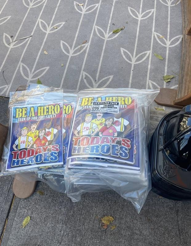 The image shows packs of "Today's Heroes" kits promoting fire safety, alongside a firefighter helmet.