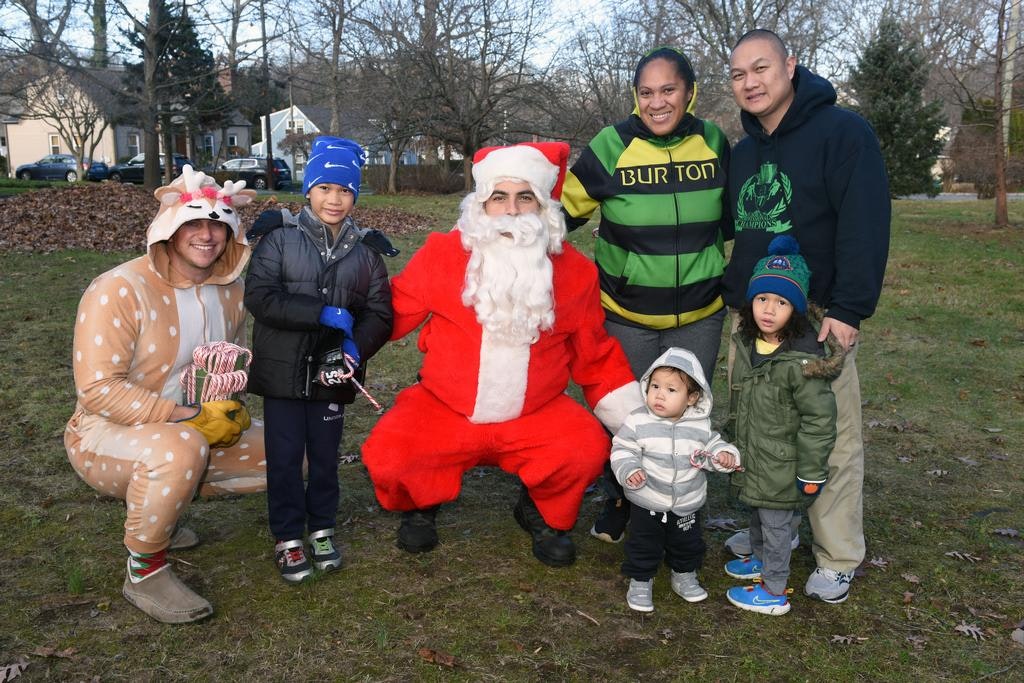 A group with someone in a Santa suit, a reindeer costume, adults, and children outdoors, holding candy canes.