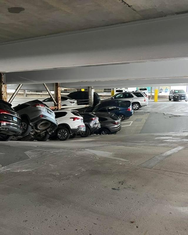 A parking garage scene showing cars stacked awkwardly, some seemingly piled up, creating a chaotic appearance.