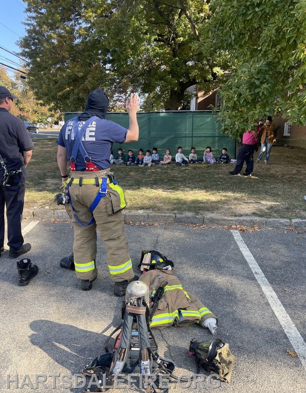 A firefighter talks to a group of children, with firefighter gear laid out nearby.