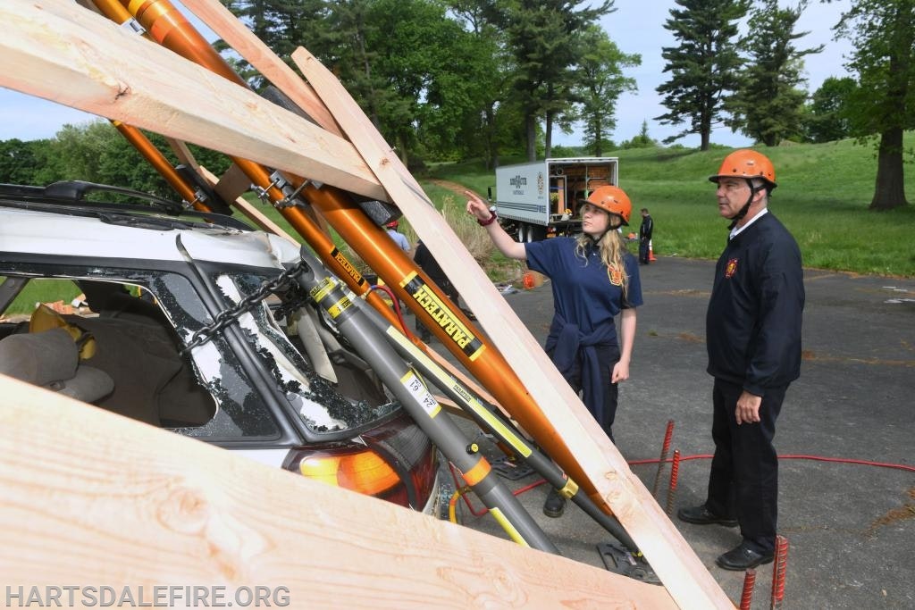 Two people in hard hats inspect a vehicle with wooden beams and tools in a training or rescue scenario.