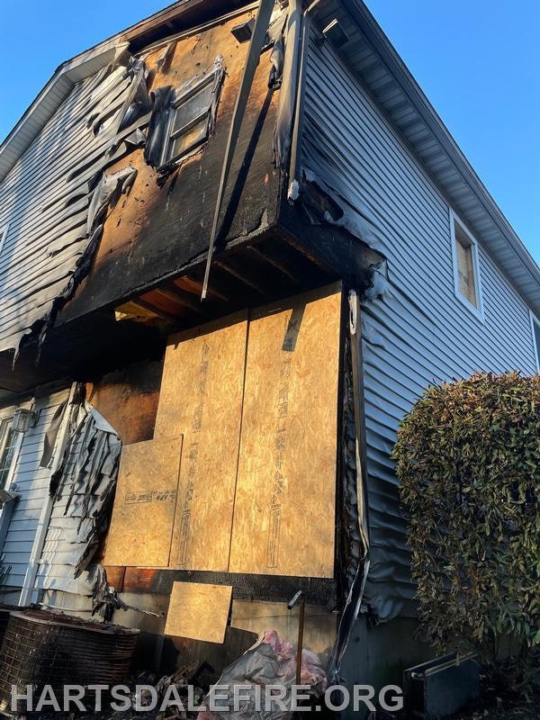A house with fire damage, including charred walls and boarded-up windows.