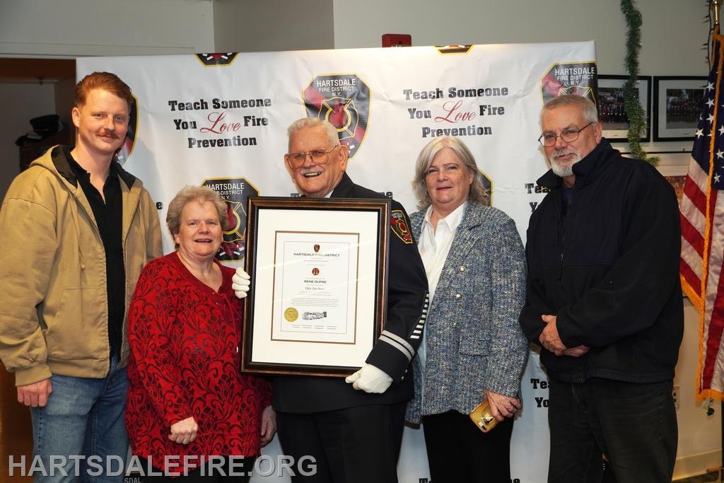 A group of five people poses with a fire prevention award in front of a backdrop promoting fire safety.