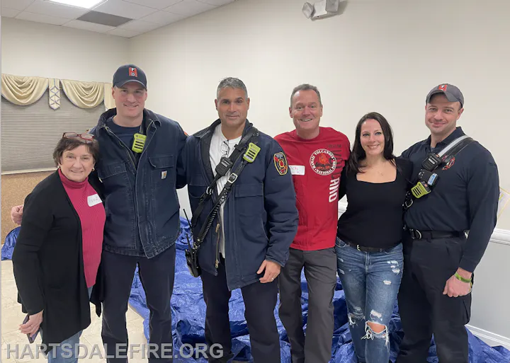 A group of six people posing together, some in firefighter gear, likely at an event or gathering related to firefighting.