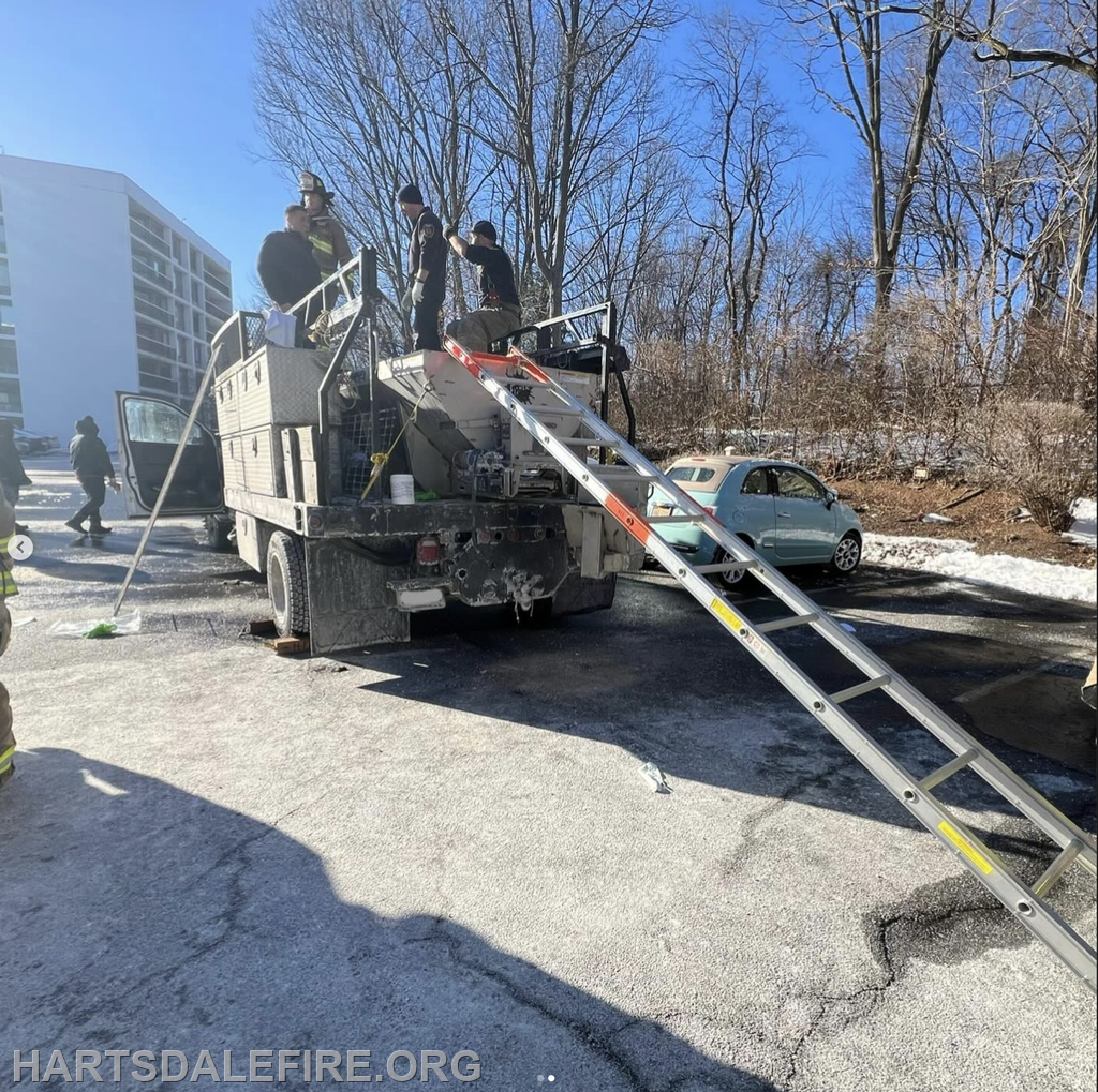 Firefighters are working on a truck with a ladder in a snowy area, while another vehicle is parked nearby.