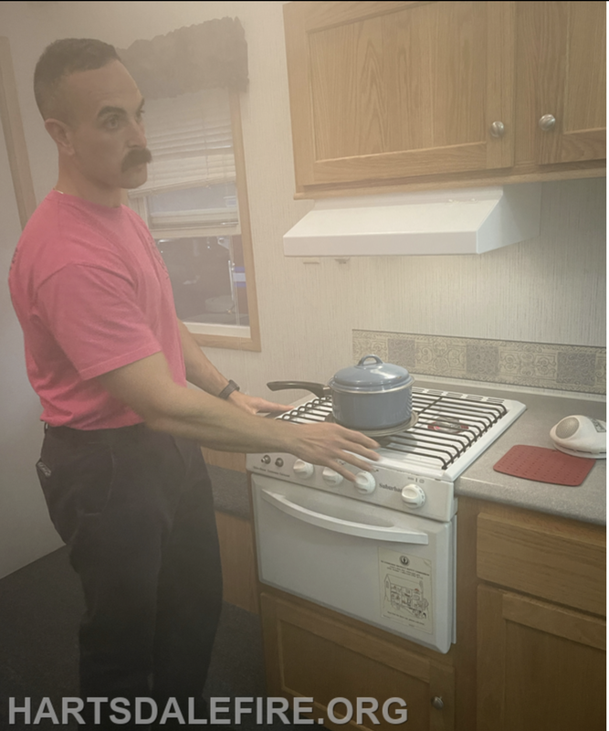 A person in a pink shirt stands by a stove with a pot, surrounded by smoke, indicating a potential cooking hazard.