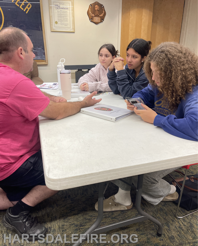 A group discussion at a table with four people, focused on a presentation or project. Conversation and collaboration are evident.