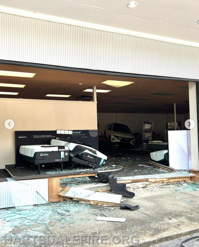 A damaged storefront with broken glass, overturned mattresses, and debris scattered on the ground. A vehicle is partially visible inside.
